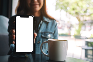 Mockup image of a beautiful woman holding and showing black mobile phone with blank screen in cafe - obrazy, fototapety, plakaty