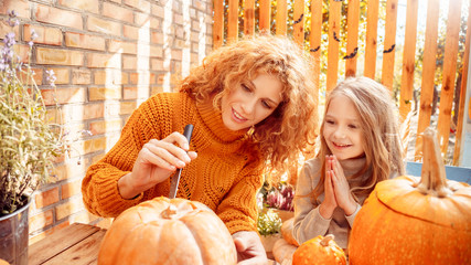 Young adult mother carving pumpkin with her little daughter