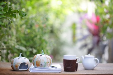 smiling white cup with old pumpkin decor and teapot and small plant pot and book on wooden table