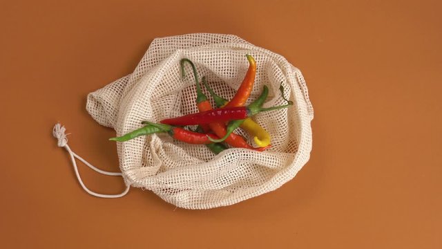 Top view of woman's hands holding red, yellow and green chilies and putting them into cotton mesh