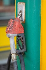 A red old fuel nozzle has dirty stain and rust. It's hang on green and yellow background.