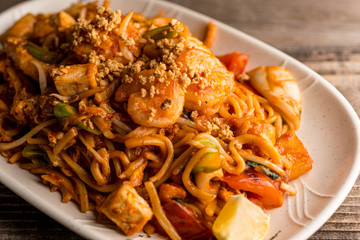 Stir fry Pad Thai with shrimp, squid, tofu, and peanuts. Served on a reclaimed wood table.