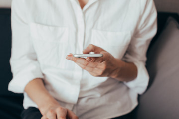 Woman hand holding white mobile phone and sitting on sofa at home.