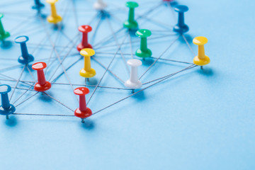 Small network of colorful pins and string, An arrangement of colorful pins linked together with string on a blue background suggesting a network of connections.