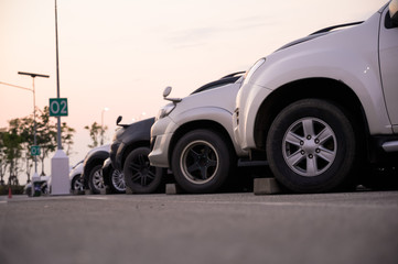 Many cars are parked in a large parking lot. Arranged in a long line Was the time when the sun was setting