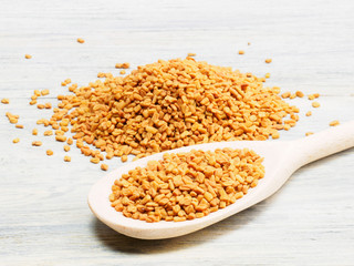 Fenugreek in spoon and on white wooden background. Indian cuisine, ayurveda, naturopathy, modern apothecary concept