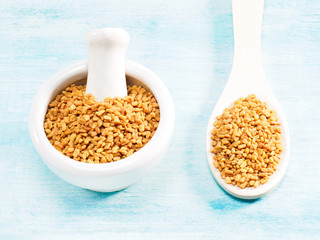 Fenugreek in white mortar and wooden spoon on a blue background. Indian cuisine, ayurveda, naturopathy, modern apothecary concept