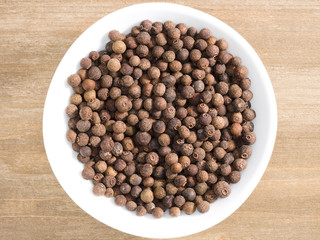 Allspice in white bowl on a brown wooden background. Indian cuisine, ayurveda, naturopathy, modern apothecary concept