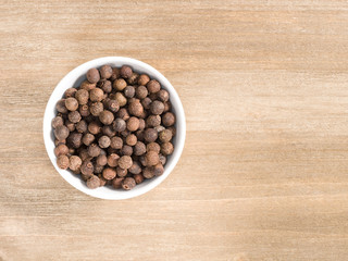 Allspice in white bowl on a brown wooden background. Indian cuisine, ayurveda, naturopathy, modern apothecary concept
