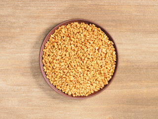 Fenugreek in clay plate and spoon on a brown wooden background. Indian cuisine, ayurveda, naturopathy, modern apothecary concept