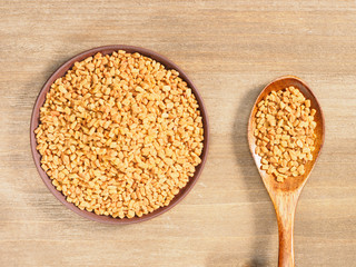 Fenugreek in clay plate and spoon on a brown wooden background. Indian cuisine, ayurveda, naturopathy, modern apothecary concept
