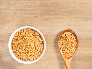 Fenugreek in white bowl and spoon on a brown wooden background. Indian cuisine, ayurveda, naturopathy, modern apothecary concept
