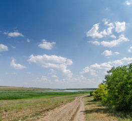 Fototapeta premium rural dirty road in green meadow and low clouds in blue sky