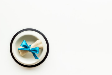 Dog's birthday concept. Chewing bones with bow in bowl on white background top view copy space