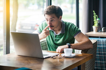 You are liar. Young angry businessman in green t-shirt sitting and looking at laptop display on...