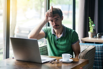 I am loser. Young sad businessman in green t-shirt sitting and looking at camera with loser gesture...