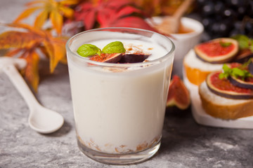 Yogurt with muesli and fig fruit in a glass, sandwich with cream cheese, figs and honey served on a small white cutting board. Healthy food concept. Autumn harvest.