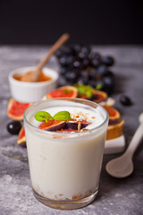Yogurt with muesli and fig fruit in a glass, sandwich with cream cheese, figs and honey on the concrete background. Healthy food concept. Autumn harvest.