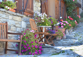Fototapeta na wymiar colorful flowers potted and chairs in front of the facade of an alpine house in a village