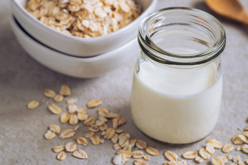 Bottle of oat milk and oat grains in bowl on table .