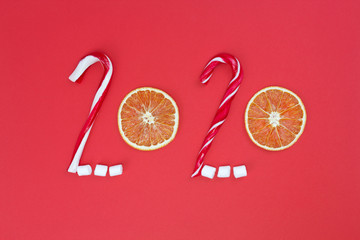Happy New Year 2020 concept. Text from candy canes, marshmallows, dried oranges on red background. ...
