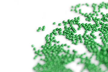 Green color seed beads scattered on a white close-up. Abstract background