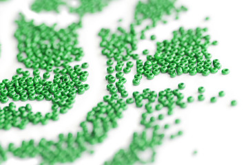Green color seed beads scattered on a white close-up. Abstract background