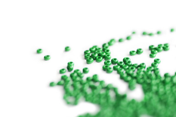 Green color seed beads scattered on a white close-up. Abstract background