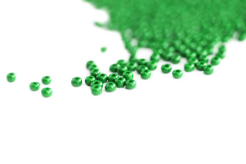 Green color seed beads scattered on a white close-up. Abstract background