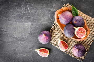 Fresh figs in rustic wood bowl top view. Cut fig fruit on dark stone table or black background with copy space.