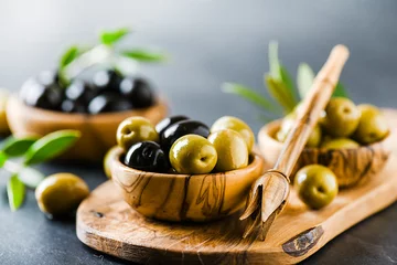 Foto op Plexiglas Fresh olives in bowl on dark stone table. Olive wood picker on rustic board. © Milan