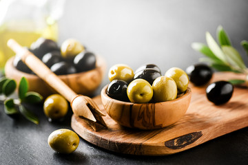 Fresh green and black original olives on black background. Olive concept on wooden cut board at dark stone table.