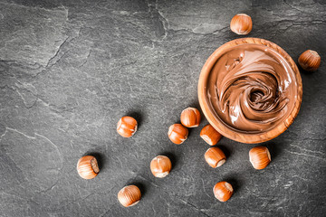 Nougat cream in olive bowl with hazelnuts on dark stone table. Hot chocolate spread concept.
