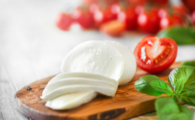 Fresh finest tomatoes on white rustic board with basil and mozzarella cheese close up or detail. - obrazy, fototapety, plakaty