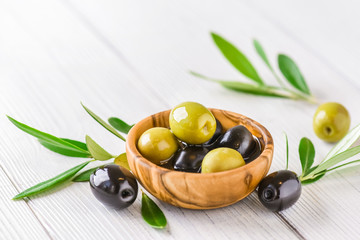 Fresh green and black olives in rustic bowl on white table. Ripe olive with leaves on light background.