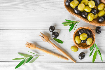 Fresh green and black olives in rustic bowl on white table. Ripe olive with leaves on light background.
