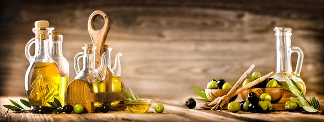 Poster Im Rahmen Frische Oliven in rustikalen Schalen auf altem Holztisch. Natives Olivenöl in Klarglasflaschen kopieren Raum. Panorama- oder Bannerkonzept. © Milan