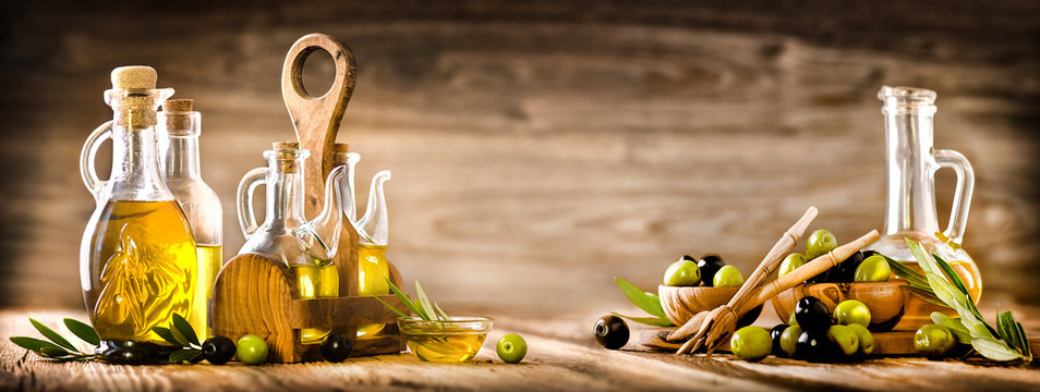 Fresh olives in rustic bowls on old wooden table. Virgin olive oil in clear glass bottles copy space.  Panorama or banner concept.