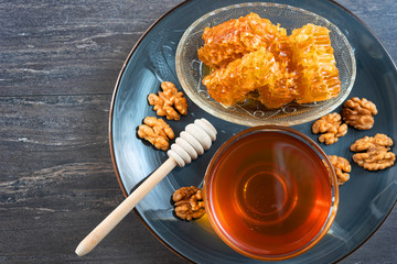 Top view of honey dipper, honey comb, walnuts and glass bowl with honey in grey dish. Close-up image. Healthy organic food concept. Grey wooden background.