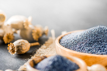 Poppy seeds in wooden bowl side view. Poppies dried heads on dark stone table.