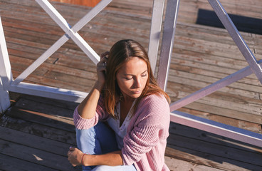 Fashionable young woman sitting on a wooden sea pier in the city center in the morning.