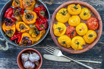 Baked red and yellow tomato and bell pepper. Tomatoes and bell peppers in a baking dish on a wooden table. A healthy and delicious vegetarian dish. Closeup, top view