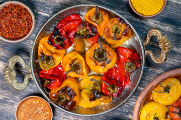 Baked red and yellow tomato and bell pepper. Tomatoes and bell peppers in a baking dish on a wooden table. A healthy and delicious vegetarian dish. Closeup, top view
