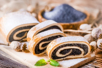 Fresh beautiful poppy roll cakes or strudel on old table. Poppies heads and seed in background