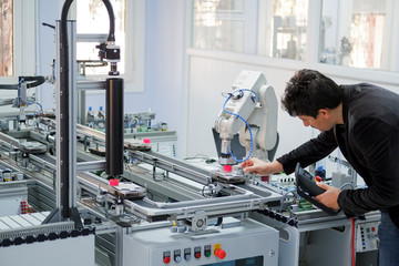 Man is holding teach panel (tablet) to control a robotic arm which is integrated on smart factory production line. industry 4.0 automation line which is equipped with sensors and robotic arm.