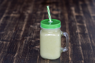 Fresh green smoothie from avocado, banana and honey in glass mug on wooden background, closeup. Concept of healthy eating