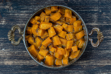 Baked yellow pumpkin with honey, anise, olive oil and spices on a plate on the wooden table. Vegetarian food. Closeup