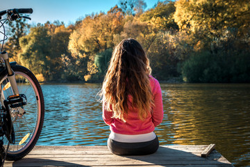girl sits on the bank of the river. bike on the river with a bag on the trunk
