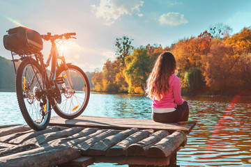 girl sits on the bank of the river. bike on the river with a bag on the trunk