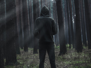 a view from the back of a lone man in a hoodie standing in a dark foggy forest